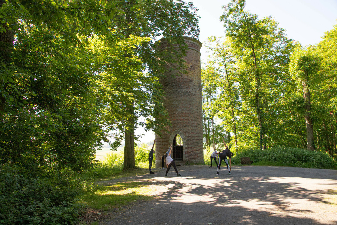 Sportifs qui procèdent à des étirements au pied d'une tour de briques rouges dans le bois de Lewarde