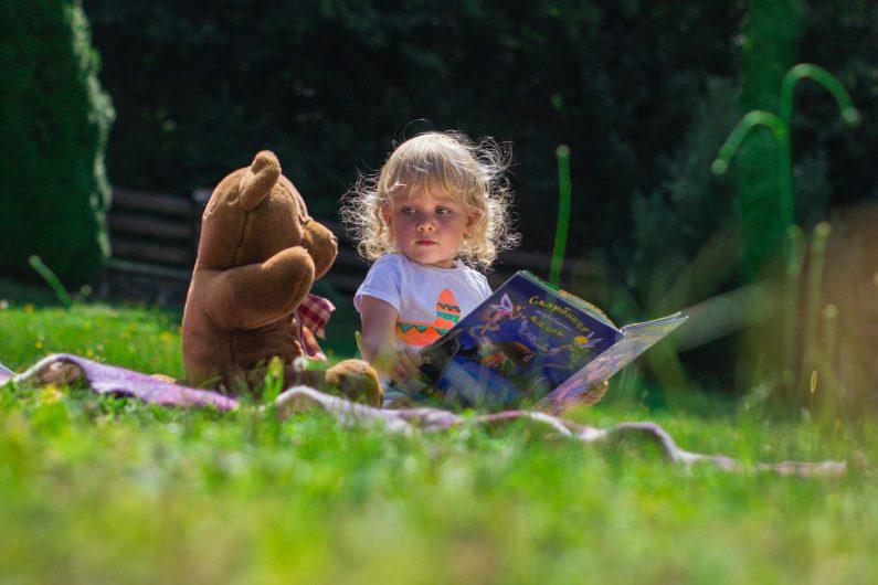 Petite fille lisant un conte à son ours en peluche